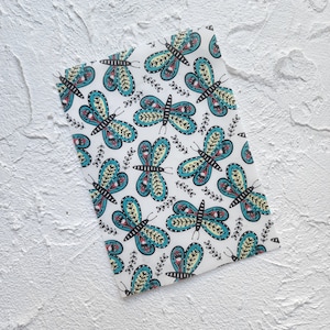 May include: White wrapping paper with a repeating pattern of teal blue butterflies with black outlines and yellow and red accents. The butterflies are surrounded by small black and white floral designs.