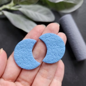 Puede incluir: Un par de pendientes de media luna azul. Los pendientes tienen una superficie texturizada.