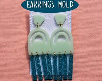Könnte beinhalten: Ein Paar grüne und türkisfarbene Ohrringe mit einem geometrischen Bogenmuster und einem Fransen aus türkisfarbenem Glitzer. Die Ohrringe werden auf einer weißen Karte mit dem Text "EARRINGS MOLD" in einem türkisfarbenen Kreis angezeigt.