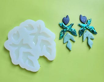 May include: A white silicone mold with four leaf-shaped cavities. Next to the mold are two teal green and black leaf-shaped earrings.
