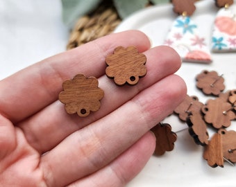 Puede incluir: Dos abalorios de madera de color marrón con forma de flor y un agujero en el centro. Los abalorios están en una mano, y hay más abalorios en el fondo.