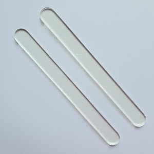 Puede incluir: Dos varillas de vidrio transparentes, rectangulares, con extremos redondeados, sobre un fondo blanco. Las varillas son paralelas, inclinadas de arriba a la izquierda hacia abajo a la derecha. Cada varilla mide unos 15 cm.