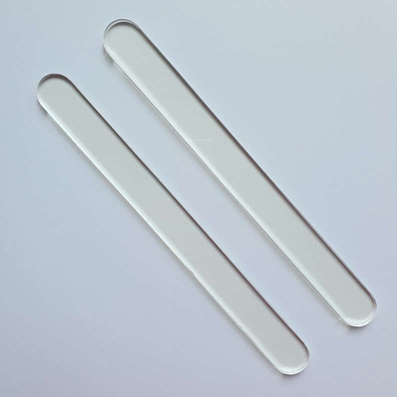 Puede incluir: Dos varillas de vidrio transparentes, rectangulares, con extremos redondeados, sobre un fondo blanco. Las varillas son paralelas, inclinadas de arriba a la izquierda hacia abajo a la derecha. Cada varilla mide unos 15 cm.