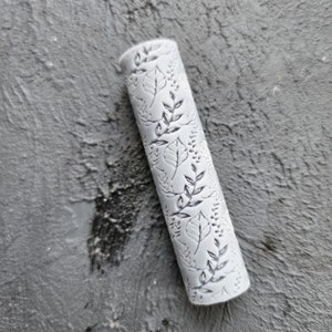 May include: A grey rolling pin with a leaf and branch design embossed on the surface.
