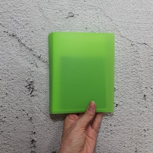 Könnte beinhalten: Ein leuchtend grüner Plastikordner mit einer transparenten Vorderseite. Der Ordner wird von einer Hand gehalten.
