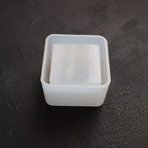 May include: A white silicone mold for making square-shaped resin crafts. The mold has two parts, a smaller inner mold and a larger outer mold.