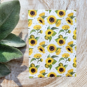 Può includere: Tessuto bianco con un motivo ripetitivo di girasoli gialli con centri neri e foglie verdi. Lo sfondo è bianco con piccoli punti neri.