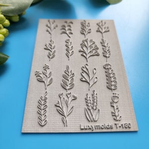 Puede incluir: Una lámina de silicona con 16 diseños diferentes de hojas y ramas para manualidades. La lámina es gris y tiene el texto "Luxymolds T-180" impreso en la esquina inferior derecha.