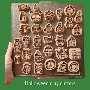May include: A set of 25 Halloween-themed cookie cutters made of brown plastic. The cutters feature various designs, including pumpkins, ghosts, bats, cats, and a skull. The cutters are arranged on a brown surface.