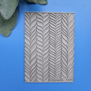 May include: Gray silicone mold with a repeating pattern of stylized leaves. The mold is labeled "Luxymolds T-121".