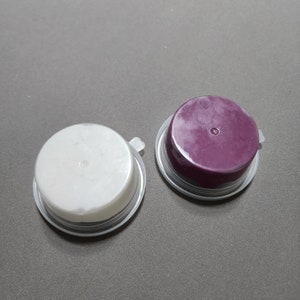 Op de afbeelding: Twee ronde containers met deksels. Eén container is wit en de andere is paars.