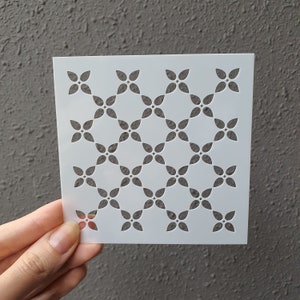 Puede incluir: Plantilla de plástico blanco con un patrón repetitivo de pequeñas formas de trébol de cuatro hojas. La plantilla está diseñada para manualidades y decoración.