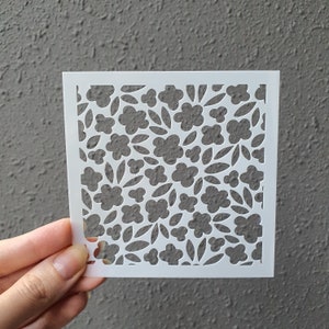 Puede incluir: Plantilla blanca con un patrón floral. El diseño presenta un patrón repetitivo de pequeñas flores y hojas.