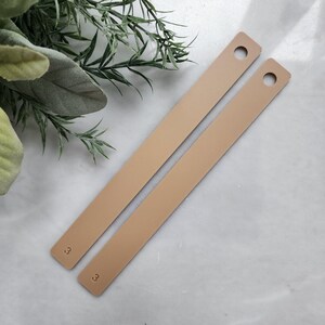 May include: Two beige leather straps with a hole at the top and the number "3" printed on the bottom of each strap.