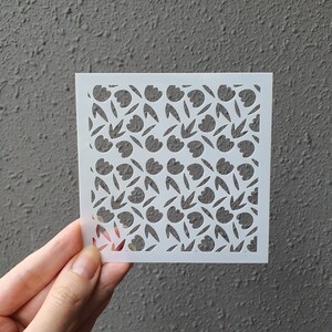 Puede incluir: Plantilla blanca con un patrón repetitivo de flores y hojas estilizadas. La plantilla está hecha de un material delgado y flexible y está diseñada para usarse con pintura u otros medios.