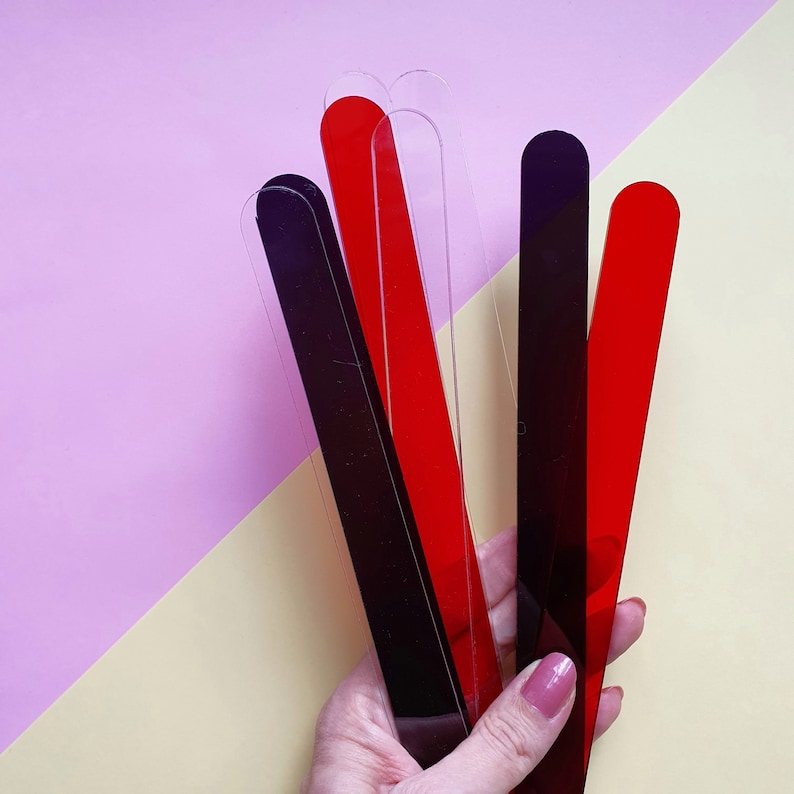 Puede incluir: Una colecci&oacute;n de varillas para remover de acr&iacute;lico transparente en rojo, negro y transparente. Las varillas son rectangulares con extremos redondeados. El fondo es una divisi&oacute;n de rosa y amarillo.