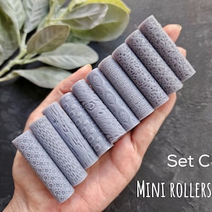 Könnte beinhalten: Satz mit acht grauen Mini-Rollern mit verschiedenen Prägemustern. Die Roller werden in einer Hand gehalten. Der Text "Set C MINI ROLLERS" ist im Bild sichtbar.