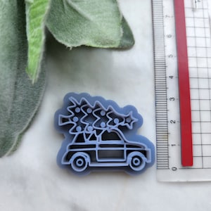 以下が含まれることがあります： クリスマスツリーが載った車の形をした薄い青色のプラスチック製のクッキーカッター。車にはツリーの頂上に星と数個のオーナメントが付いている。