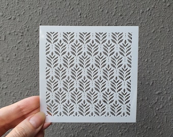May include: White stencil featuring a repeating pattern of stylised leaves and dots. The stencil is made from a thin, flexible material.