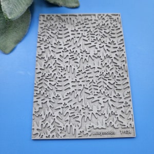 Puede incluir: Un molde de silicona gris con un patrón repetitivo de hojas. El molde está etiquetado como "Luxymolds T-134".