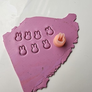 Op de afbeelding: Een roze polymeerkleioppervlak met meerdere indrukken van een konijnenvorm gemaakt met een roze plastic konijnenkoekjesuitsteker.