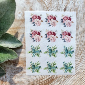 Könnte beinhalten: Eine Bogen mit 12 Blumenaufklebern. Sechs Aufkleber zeigen rosa und burgunderfarbene Rosen mit grünen Blättern. Sechs Aufkleber zeigen grüne Eukalyptusblätter.