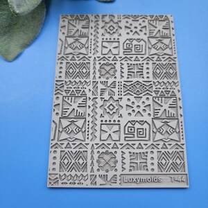 Puede incluir: Un molde de silicona gris con un patrón geométrico. El molde es rectangular y tiene un diseño en relieve de varias formas y patrones. El texto "Luxymolds T-44" está impreso en la esquina inferior derecha.