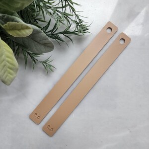May include: Two beige leather straps with holes and the text "2.5" printed on them.