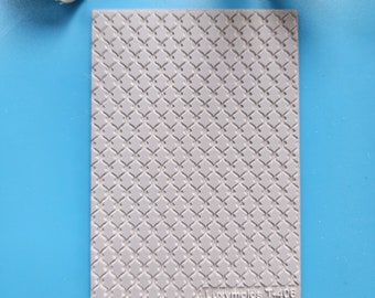 May include: A rectangular, light gray mold with a repeating diamond pattern. The mold has a textured surface and the text "Luxymolds T-406" is printed on the bottom right corner. The mold is on a blue surface.
