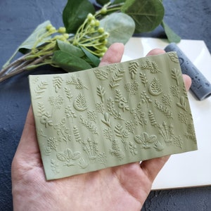Può includere: Timbro in silicone verde con una varietà di motivi di foglie e fiori. Il timbro è tenuto in una mano ed è pronto per essere utilizzato per progetti di artigianato.