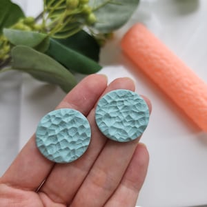 May include: A pair of light blue round earrings with a textured surface.