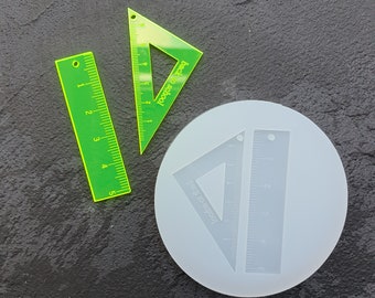 May include: A silicone mold for making resin crafts. The mold features two shapes: a ruler and a triangle. The triangle has the text "Back to School" on it. The mold is white and the shapes are clear.