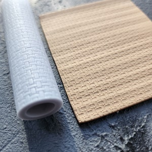 May include: A white plastic rolling pin with a brick pattern and a beige textured rolling mat. Both are used for creating decorative patterns on fondant or clay.