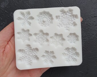 Op de afbeelding: Witte siliconen mal met negen sneeuwvlokontwerpen. De mal is gemaakt van flexibel siliconen en is perfect voor het maken van chocolade, snoep of zeep.