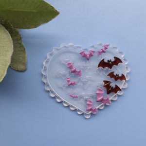 May include: A heart-shaped silicone mold with a scalloped edge. The mold is filled with small bat shapes in pink and brown.