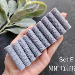 Pode incluir: Conjunto de dez mini rolos de massa cinzentos com diferentes padrões em relevo. Os rolos estão dispostos em uma fila em uma mão. O texto "Set E MINI ROLLERS" é visível no canto inferior direito da imagem.