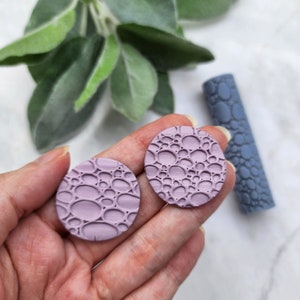 May include: Two round, purple clay earrings with a textured, bubble-like pattern.