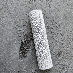 May include: A white rolling pin with a textured surface pattern of overlapping circles. The rolling pin is made of a hard plastic material.