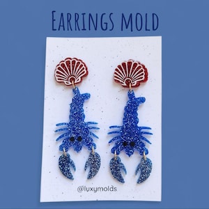 Könnte beinhalten: Zwei Paar Ohrringe mit einem blauen Hummer-Design mit Glitzerakzenten. Jeder Ohrring hat eine rot-weiße Muschelform. Der Text "Earrings MOLD" steht oben. Unten im Bild steht der Text "@luxymolds".