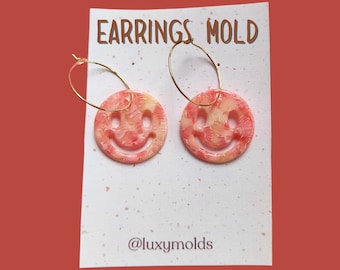 Può includere: Un paio di orecchini a cerchio dorati con un ciondolo a forma di smiley rosa e giallo. Gli orecchini sono su una carta bianca con il testo "EARRINGS MOLD" e "@luxymolds".
