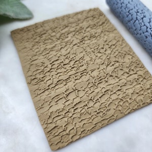 May include: A close-up of a brown textured surface with a raised pattern. The surface is made of clay and has a rough, uneven texture.