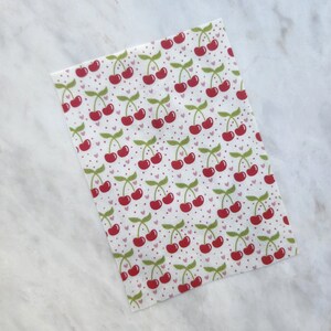 May include: White fabric with a repeating pattern of red cherries with green stems and leaves. The background has small pink hearts and white dots.