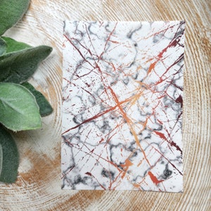 May include: A white background with a marble pattern and splashes of copper and red paint.