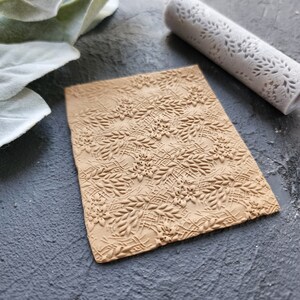 May include: A brown textured rolling pin with a floral design. The rolling pin is made of silicone and is used for creating decorative patterns on fondant, clay, or dough.