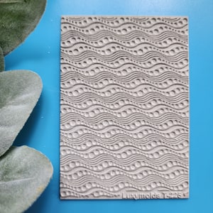 May include: A gray silicone mold with a wavy pattern of circles. The mold is textured and has the text "Luxymolds T225" in the bottom right corner.