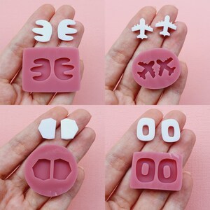 Puede incluir: Cuatro moldes de silicona para hacer pendientes. Los moldes son de color rosa y presentan diferentes formas, incluyendo alas, aviones y círculos.