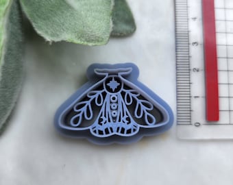 May include: A purple plastic cookie cutter shaped like a moth with intricate details. The moth has a star on its head and a pattern of circles and lines on its body.