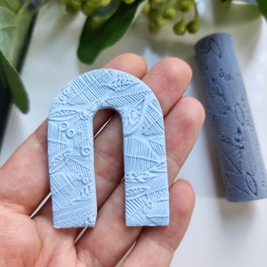 Può includere: Un arco in argilla polimerica blu chiaro con un motivo a foglie. L'arco è alto circa 5 cm e largo 2,5 cm.