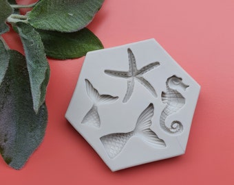 May include: A white silicone mold with four cavities shaped like a starfish, a seahorse, and two mermaid tails.