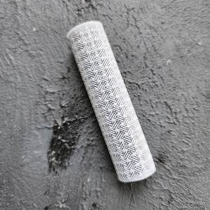 May include: A white cylinder with a black and white geometric pattern. The cylinder is lying on a gray surface.